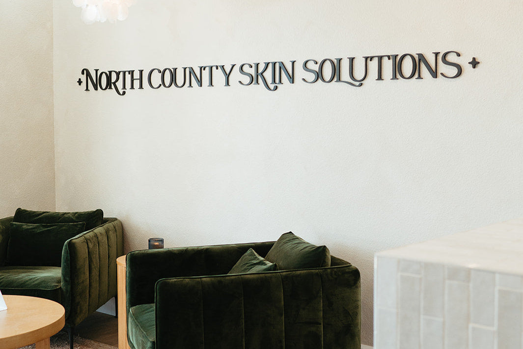 Green velvet couches in a room with 'North County Skin Solutions' wall text.