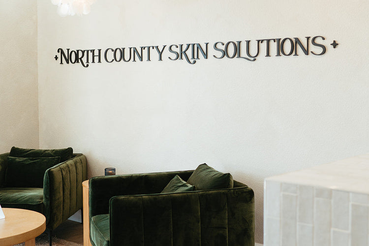 Green velvet couches in a room with 'North County Skin Solutions' wall text.