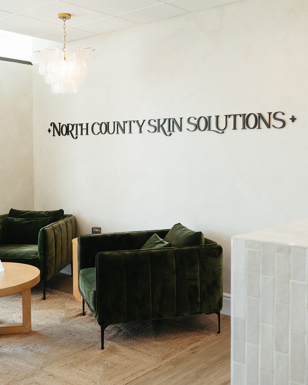 Waiting area with green chairs and a wall sign reading 'North County Skin Solutions' in a modern office setting.