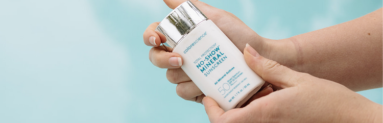 Hand holding a bottle of 'No Show' mineral sun screen with a light blue background