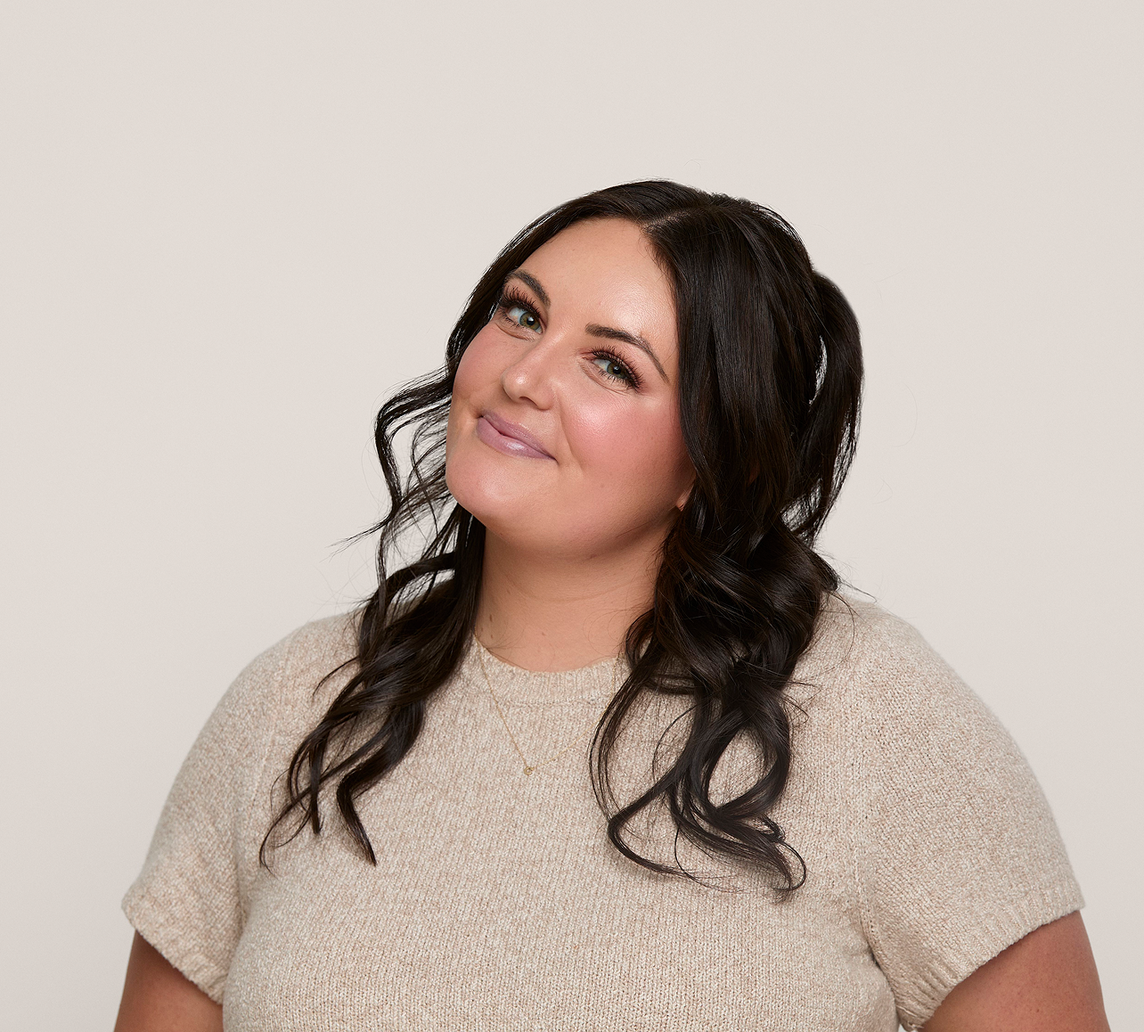 Woman with long, wavy hair wearing a beige sweater against a plain background