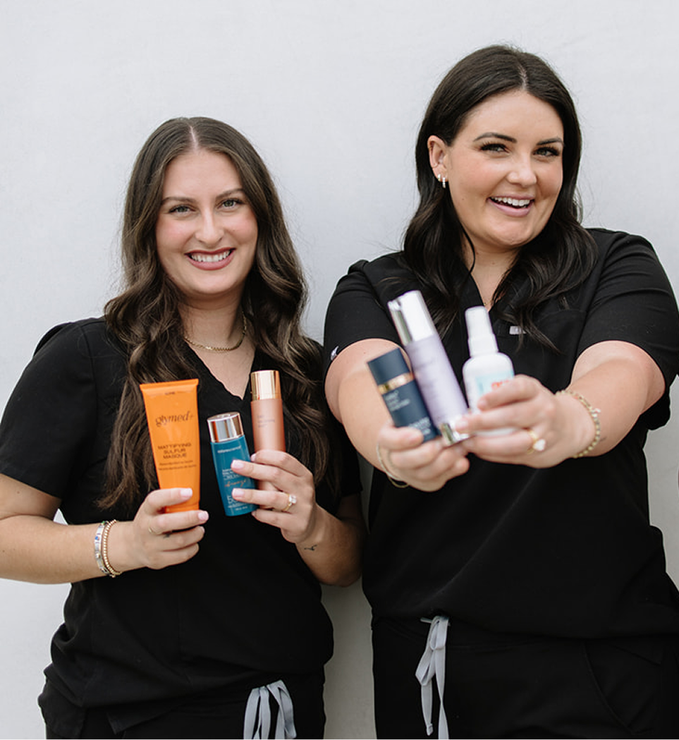 Two women holding skincare products against a plain background